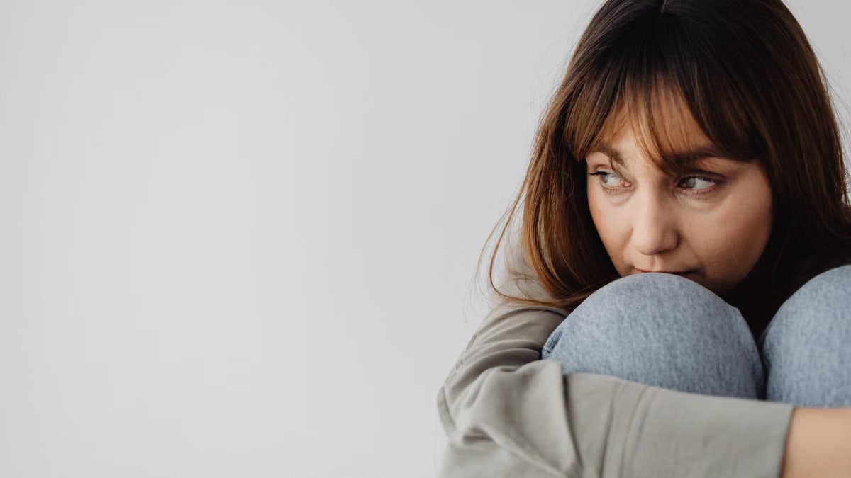 Close-up of a woman hugging her knees, gazing thoughtfully indoors